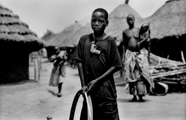 An Acholi boy playing with an old bicycle wheel between the camp huts. He was born and has been brought up in the camp, there is little access to education for him and he knows little of how the Acholi people used to live their lives.