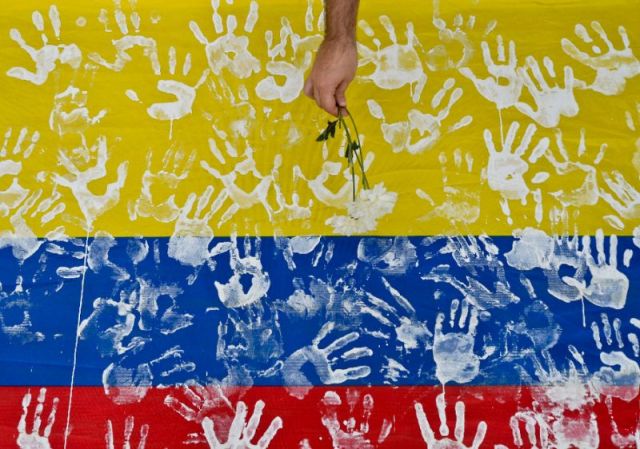 A man places a flower on a Colombian flag (Photo: Luis Robayo / AFP)